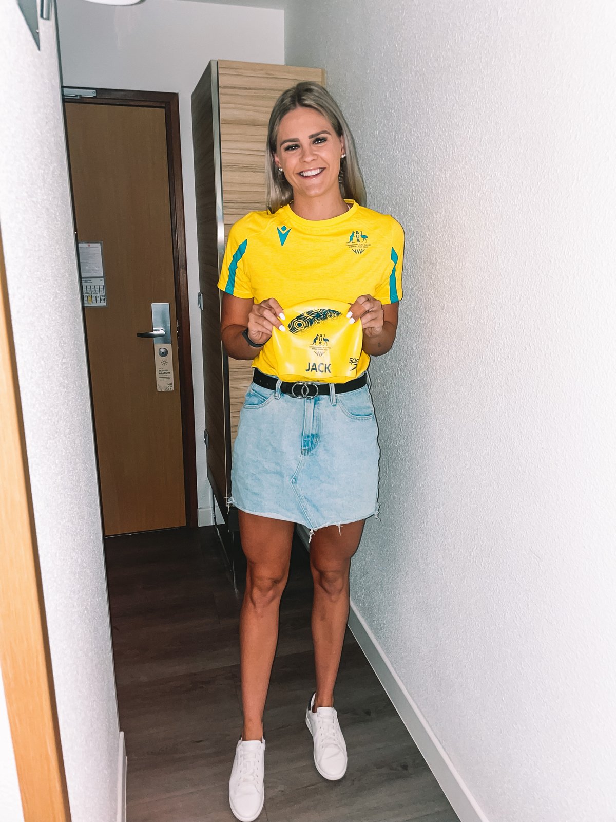 Shayna Jack in an Australian team shirt, holding up her yellow Australian swim cap with JACK on it.