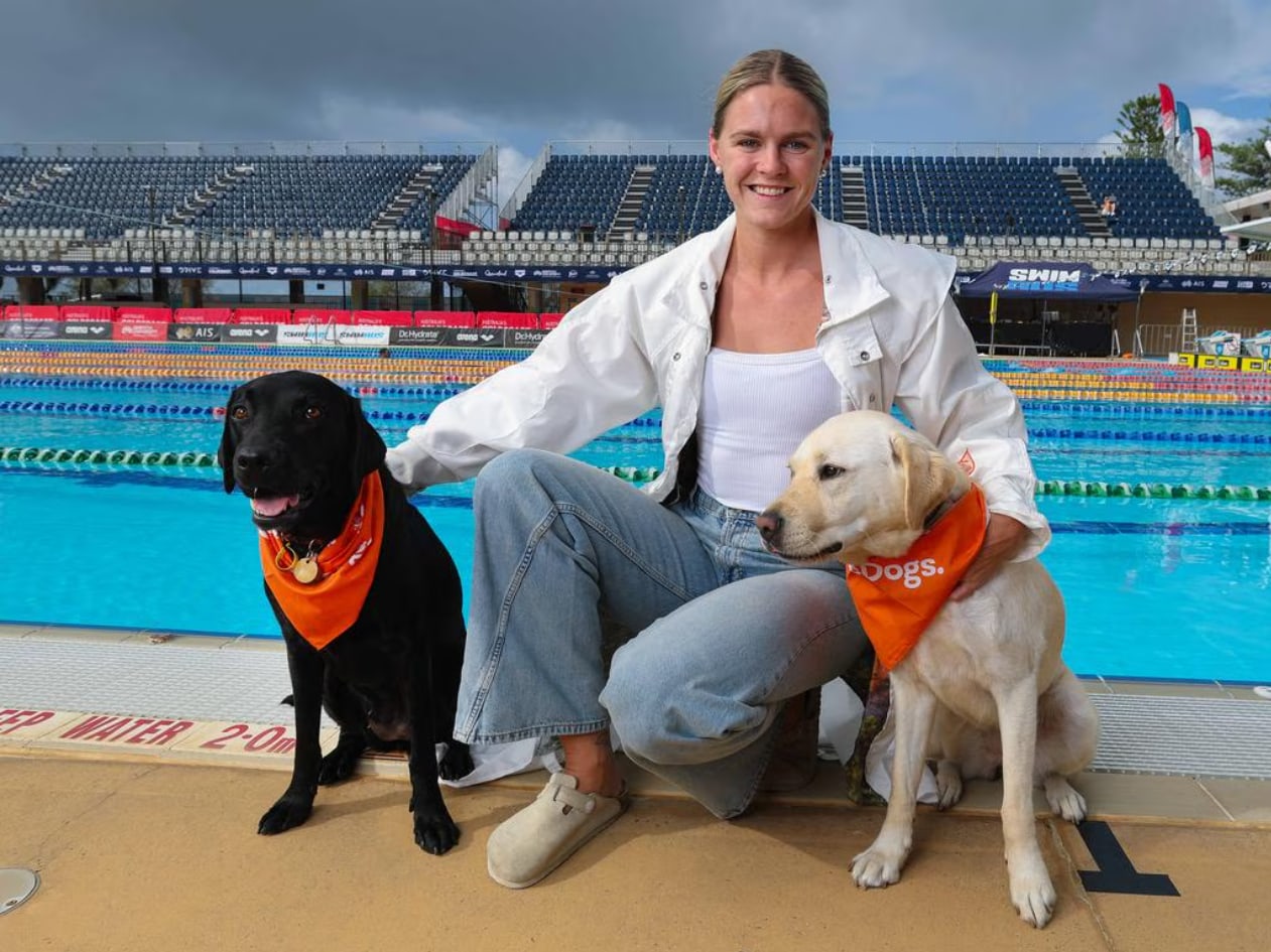 Shayna Jack sitting poolside with two Guide Dogs puppies in orange Guide Dogs bandanas.