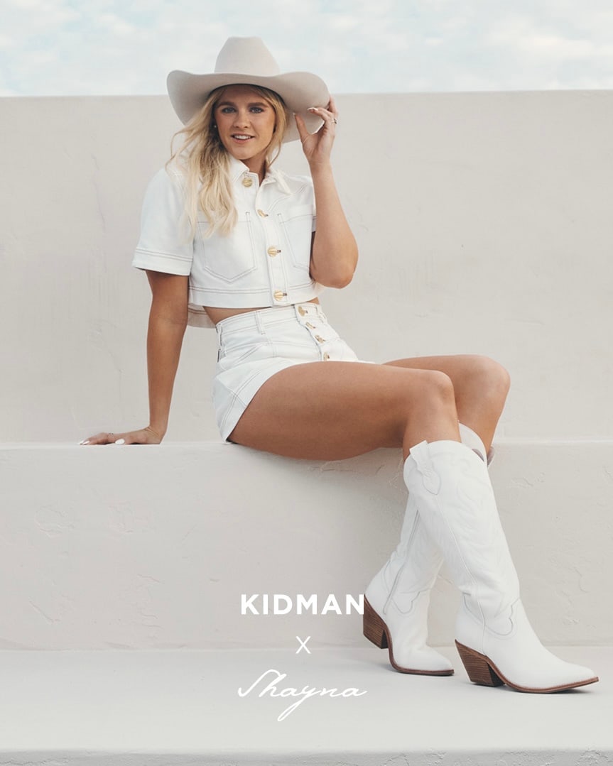 Shayna Jack in a white outfit, cowboy hat and boots, seated on a white wall for the Kidman campaign.