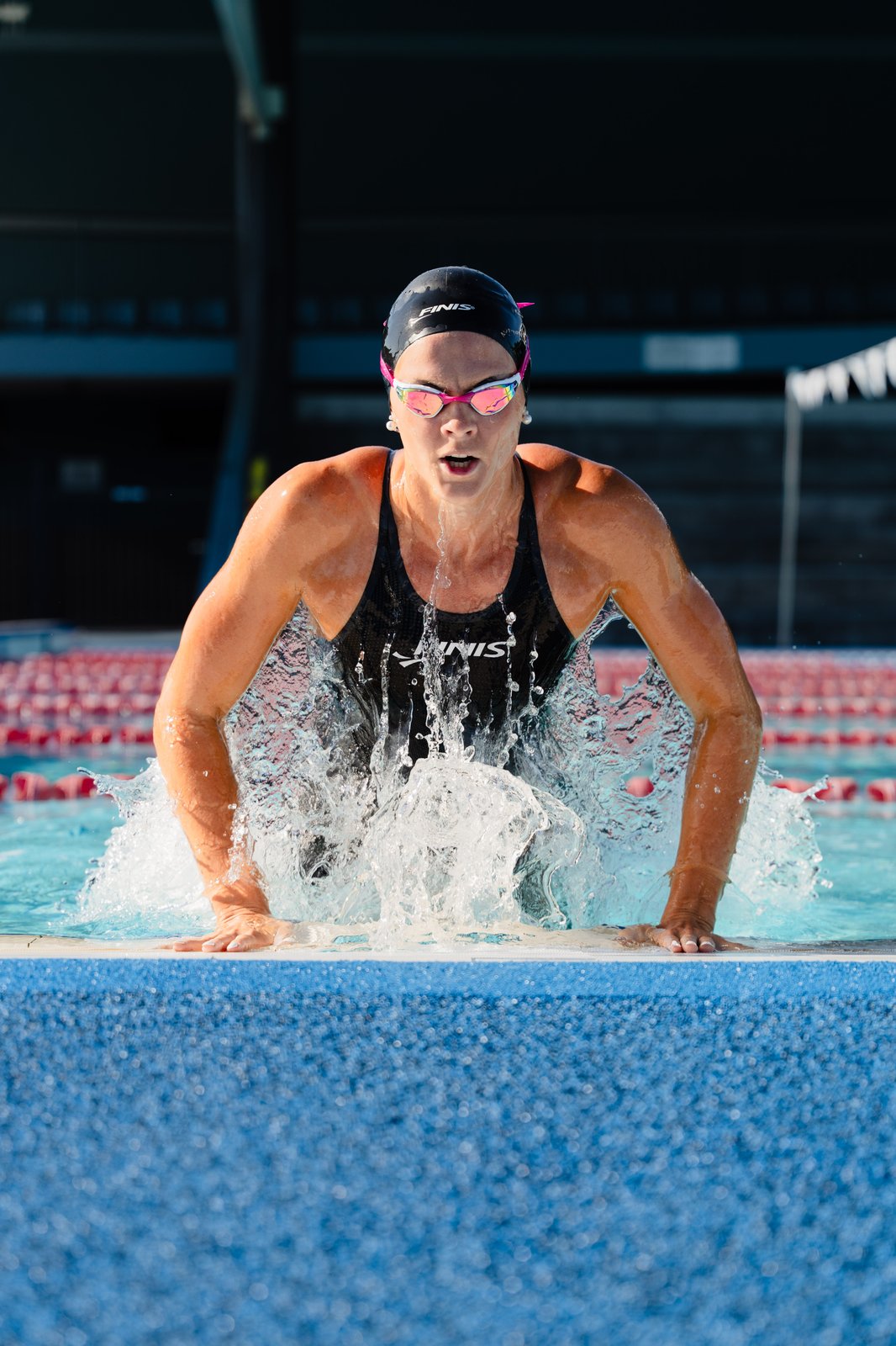 Shayna Jack surging out of the water at the end of a pool lane, wearing a cap and goggles.