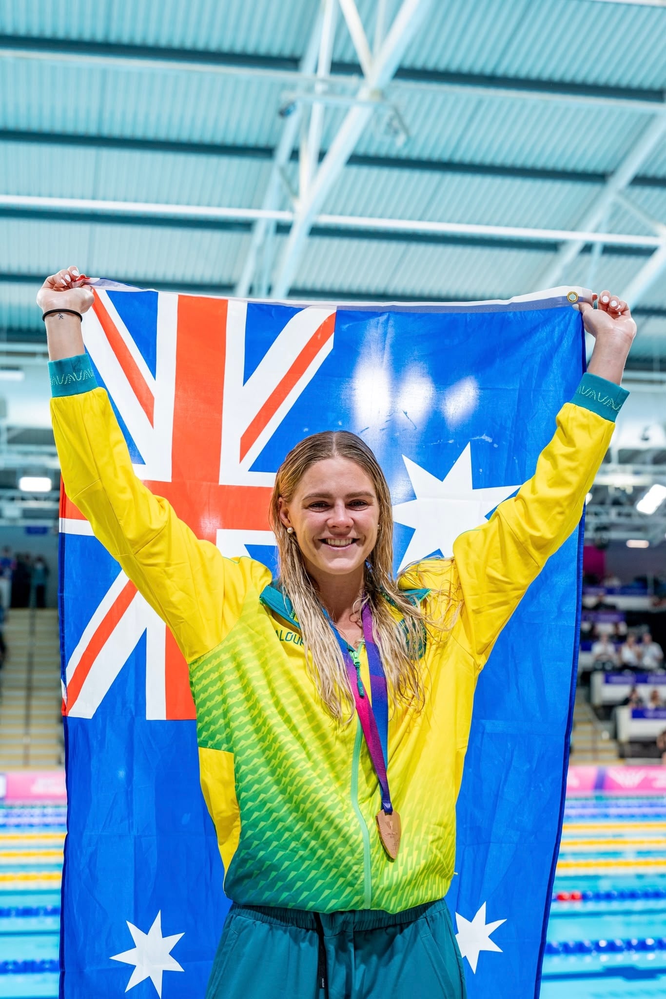 Shayna Jack holding an Australian flag above her head at the side of a pool, wearing a medal.