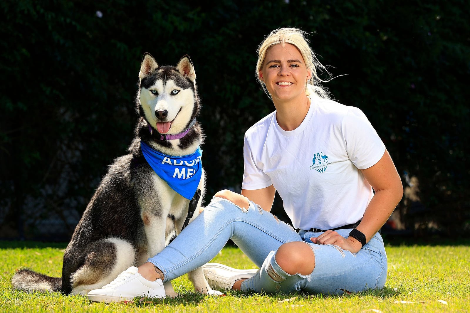 Shayna Jack sitting on the grass beside a husky wearing an RSPCA “Adopt me” bandana.