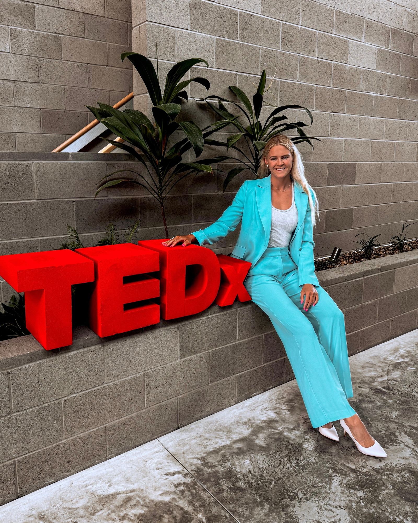 Shayna Jack in a turquoise suit, sitting beside the red TEDx letters.