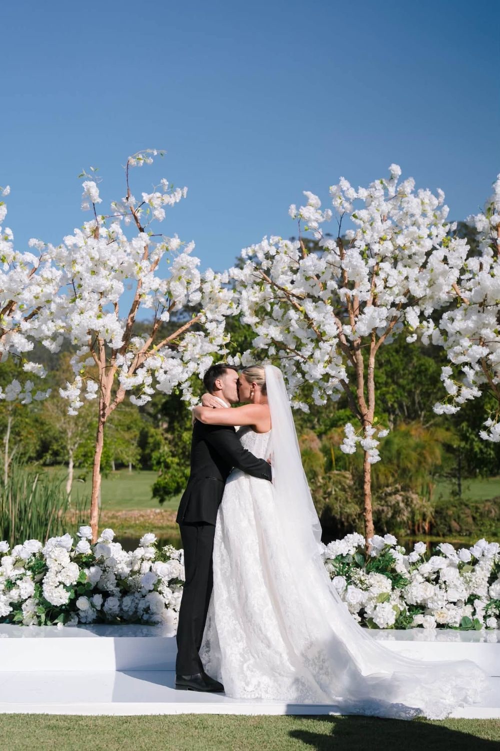 Shayna and Joel kiss at the end of their ceremony, beneath white blossom trees.